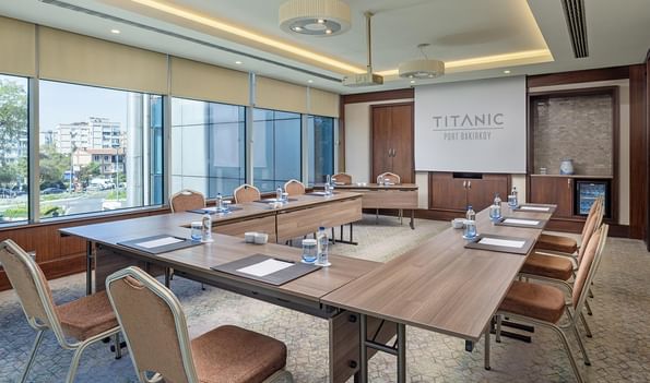 Aegean toplantı salonunda projeksiyon perdesiyle U şeklinde masa kurulumu ve şehir manzaralı geniş pencereler Titanic Port Bakırköy’de.