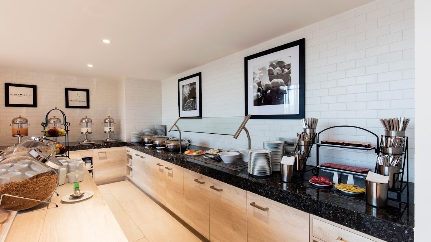 Buffet at Fiesta Inn Express Cancún Cumbres with food warmers on a counter by the tiled wall, Cancun hotel breakfast