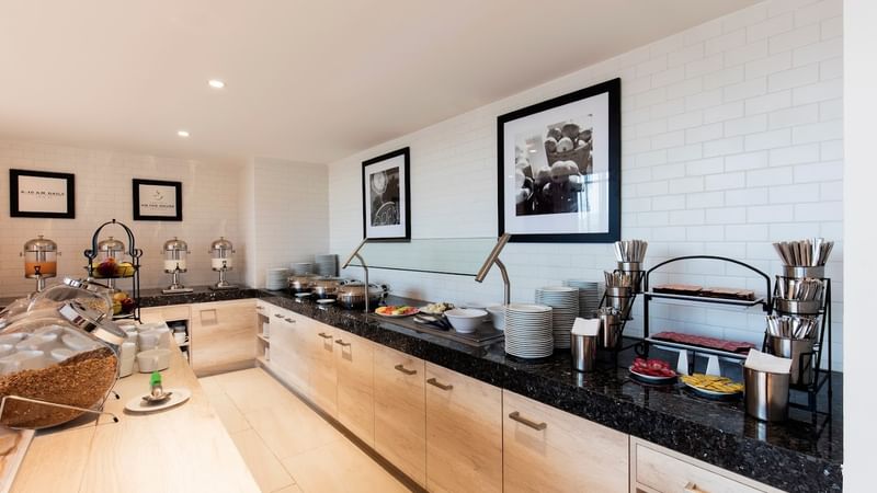 Buffet at Fiesta Inn Express Cancún Cumbres with food warmers on a counter by the tiled wall, Cancun hotel breakfast