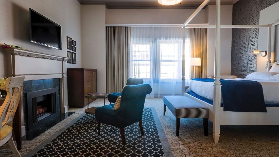 Teal armchairs by a marble fireplace under a wall-mounted TV in Loft Fireplace Suite at Warwick San Francisco