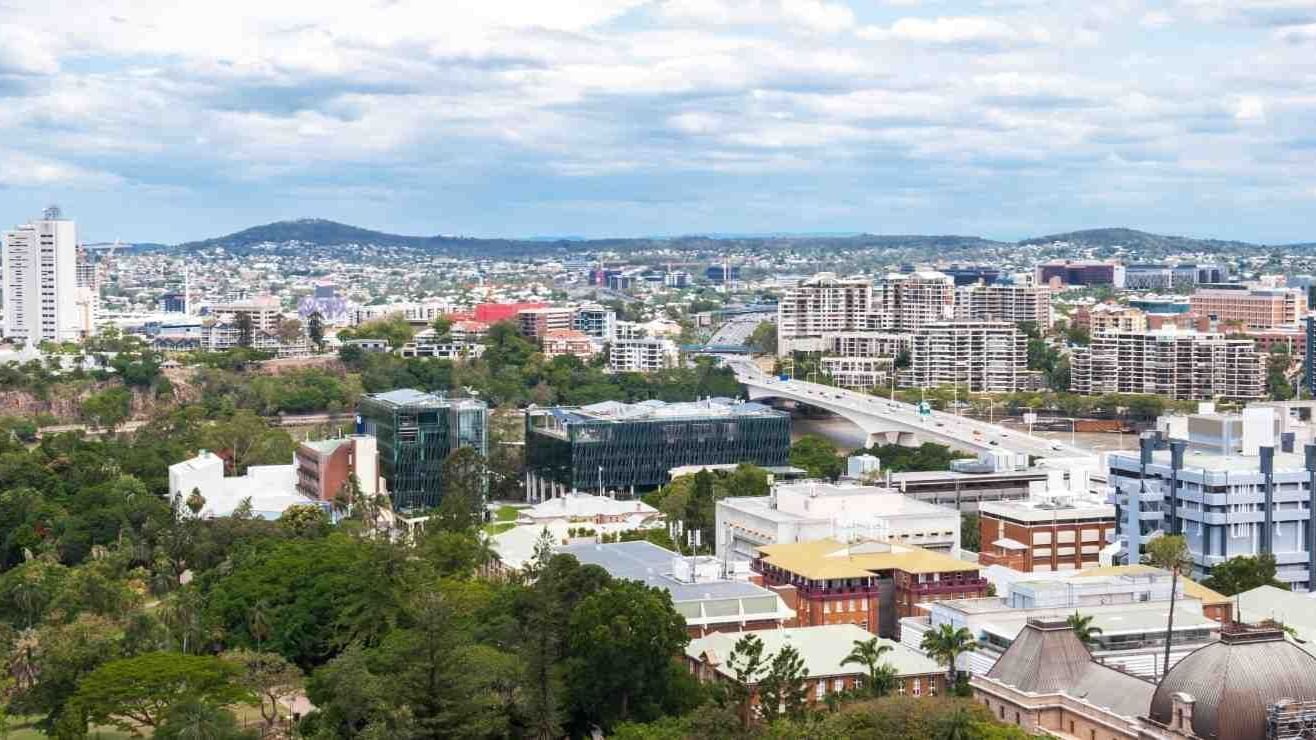 Panoramic cityscape view showing urban buildings, green trees, and distant hills under a partly cloudy sky at StudentLiving - on Margaret