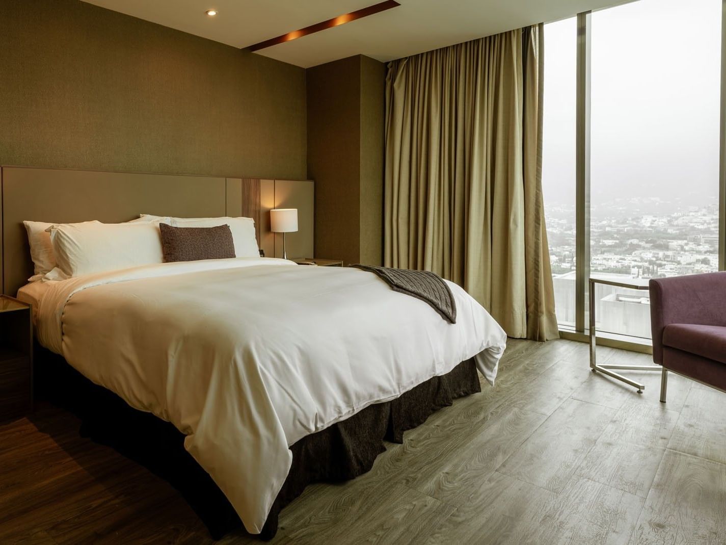 King Junior Suite with a large window overlooking the city view and a purple chair at Camino Real Fashion Drive, Monterrey