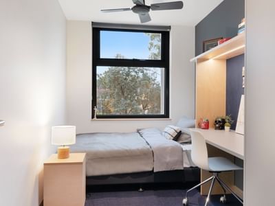 Single room with bed, desk, chair, window, and ceiling fan at La Trobe University - North and South Apartments.