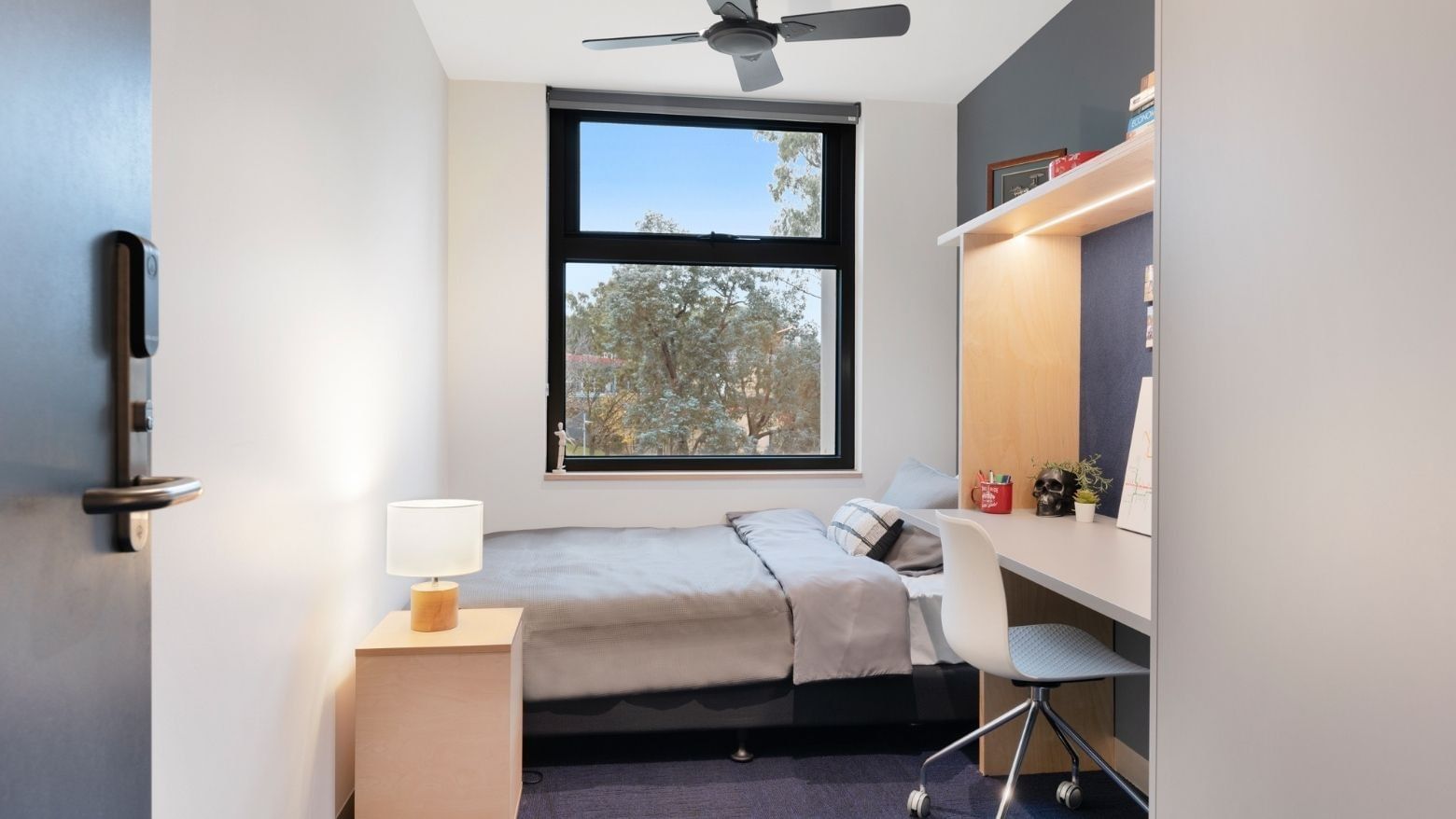 Single room with bed, desk, chair, window, and ceiling fan at La Trobe University - North and South Apartments.