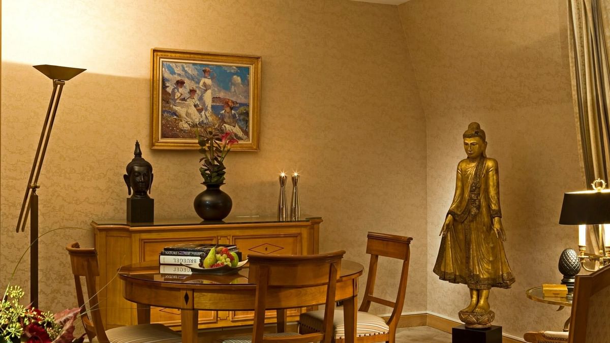 Golden Buddha statue placed by a round dining table under soft light in Royal Suite at Warwick Grand-Place Brussels