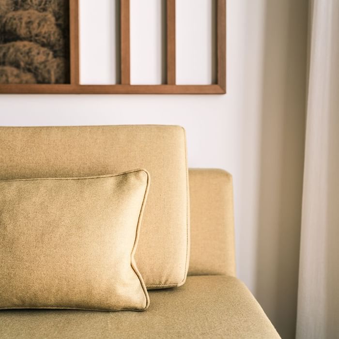 Plush tan couch with a pillow, partial view of a picture frame above at Falkensteiner Hotel Montafon