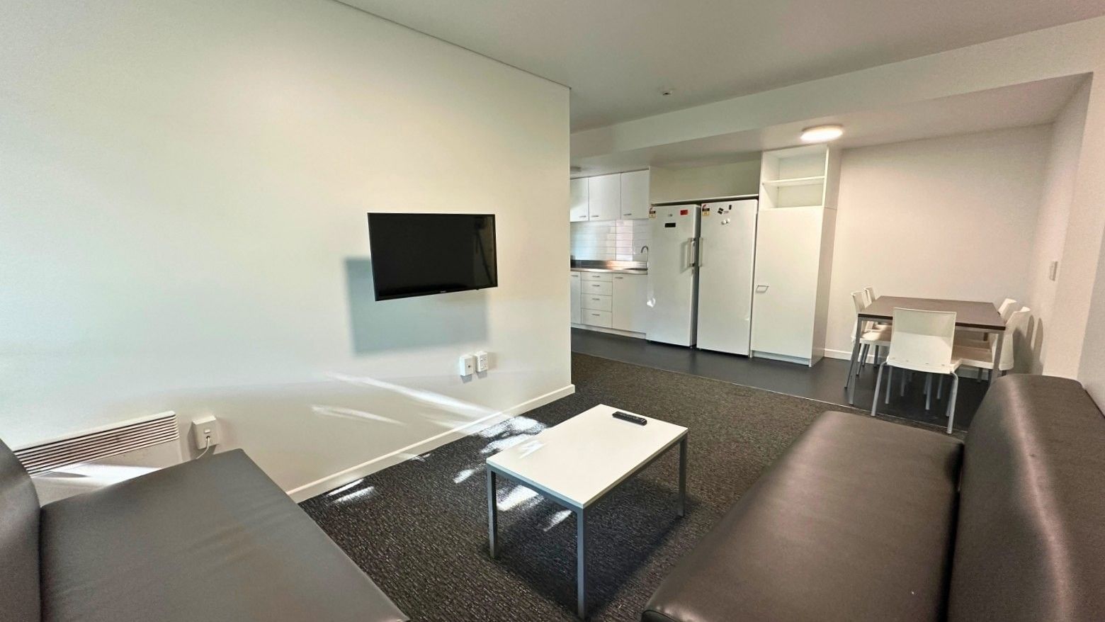 Black couches, white coffee table, and flat screen TV in a student accommodation.