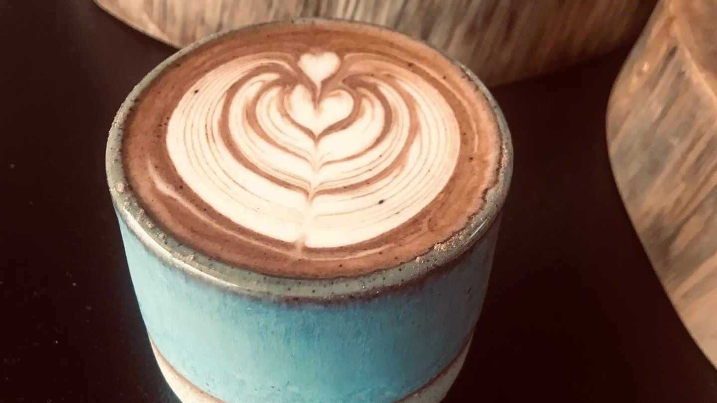 Hot coffee with heart latte art in a blue ceramic cup by a wooden block on a table at the Elysium Manly