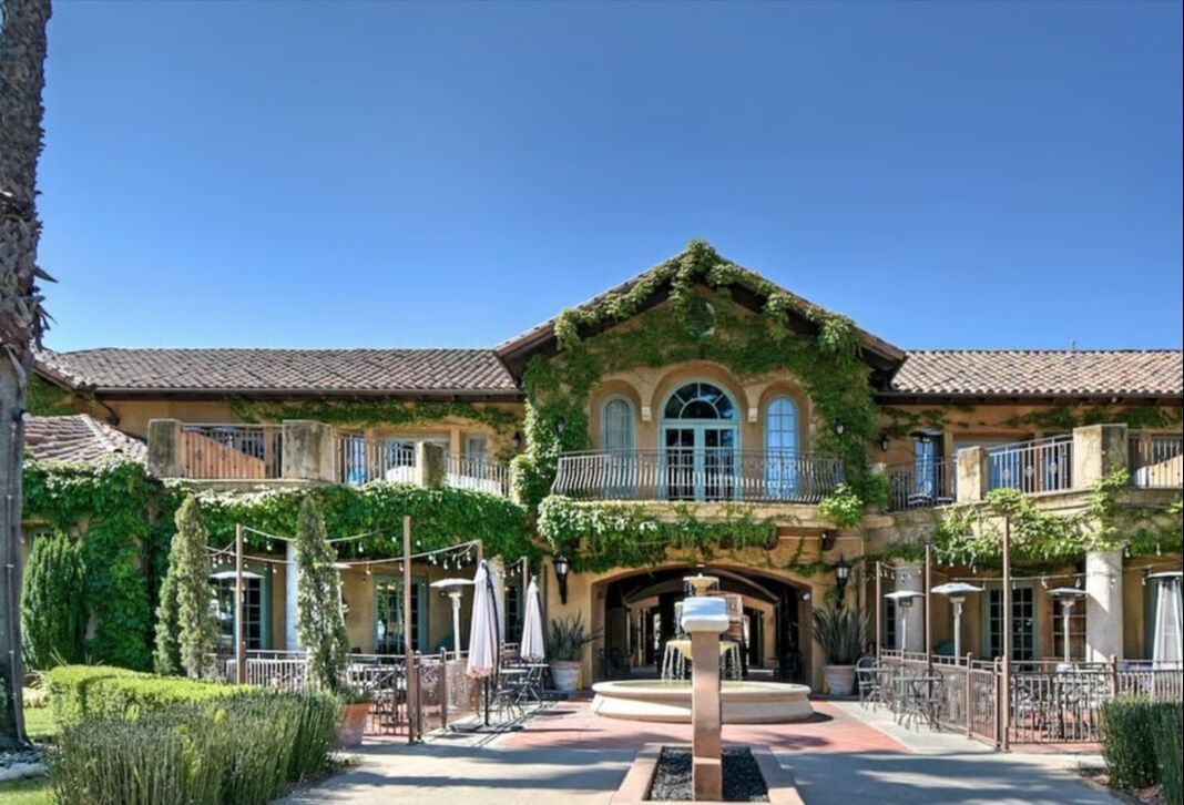 A large building with ivy growing on it and a patio area with tables and chairs.