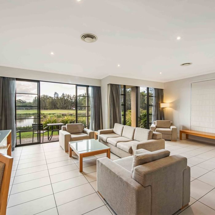 Three Bedroom Apartment living room with a lake view through large windows, sofas, and a TV at Mercure Kooindah Waters