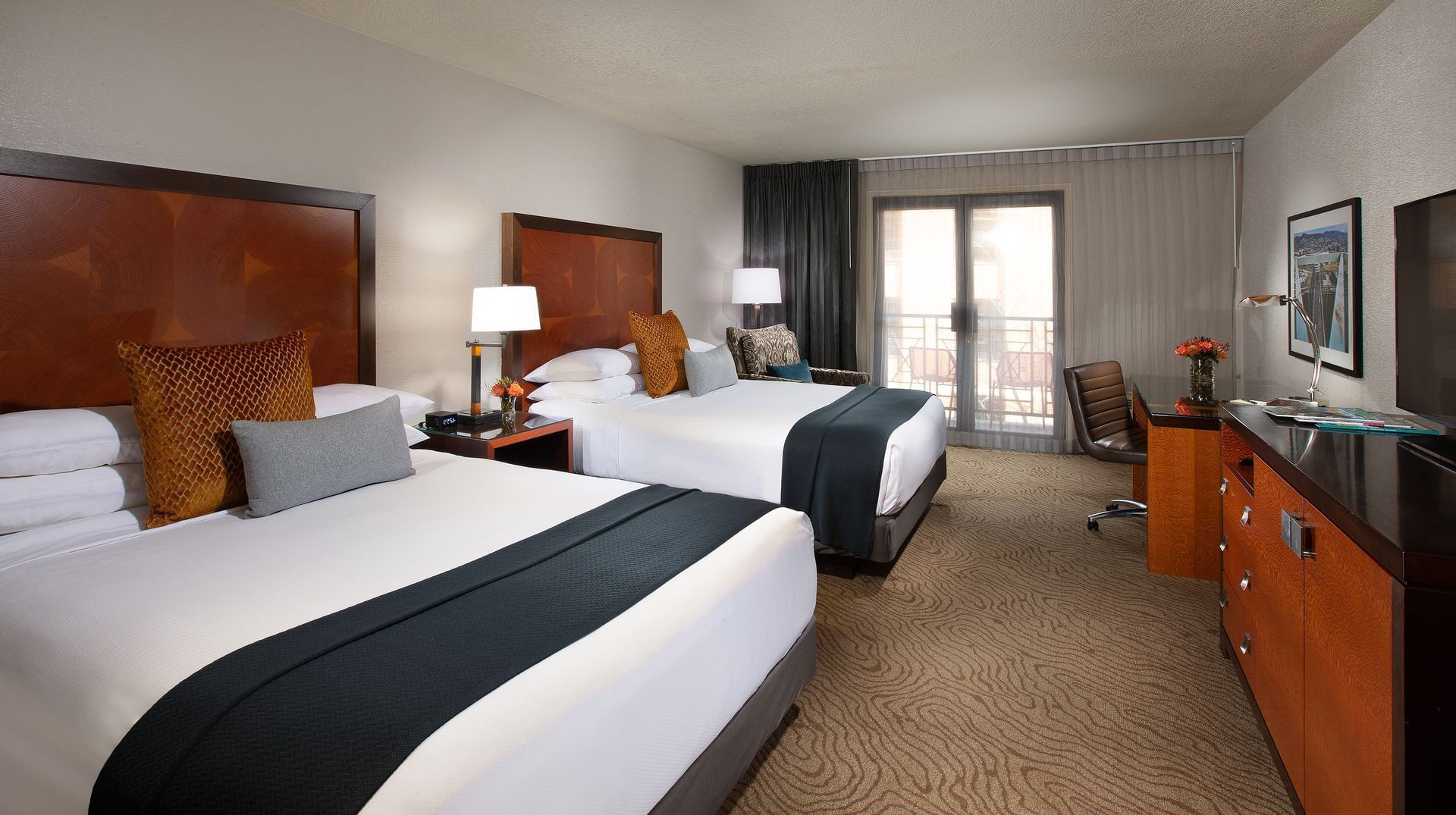 A hotel room with two double beds, a desk, and a balcony door.