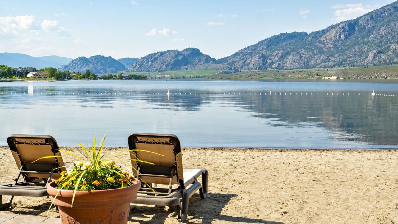 Two beach chairs on sand facing lake and mountains