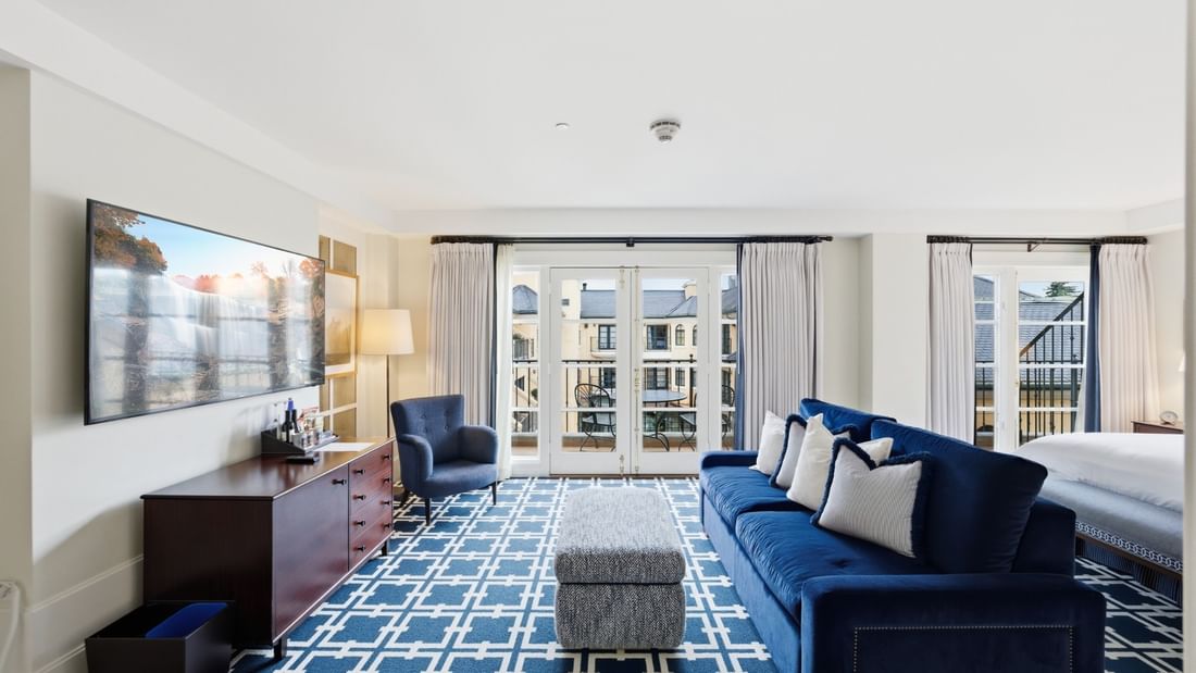 Spacious suite with blue velvet sofa, patterned rug, and balcony doors at el PRADO Hotel in Palo Alto.