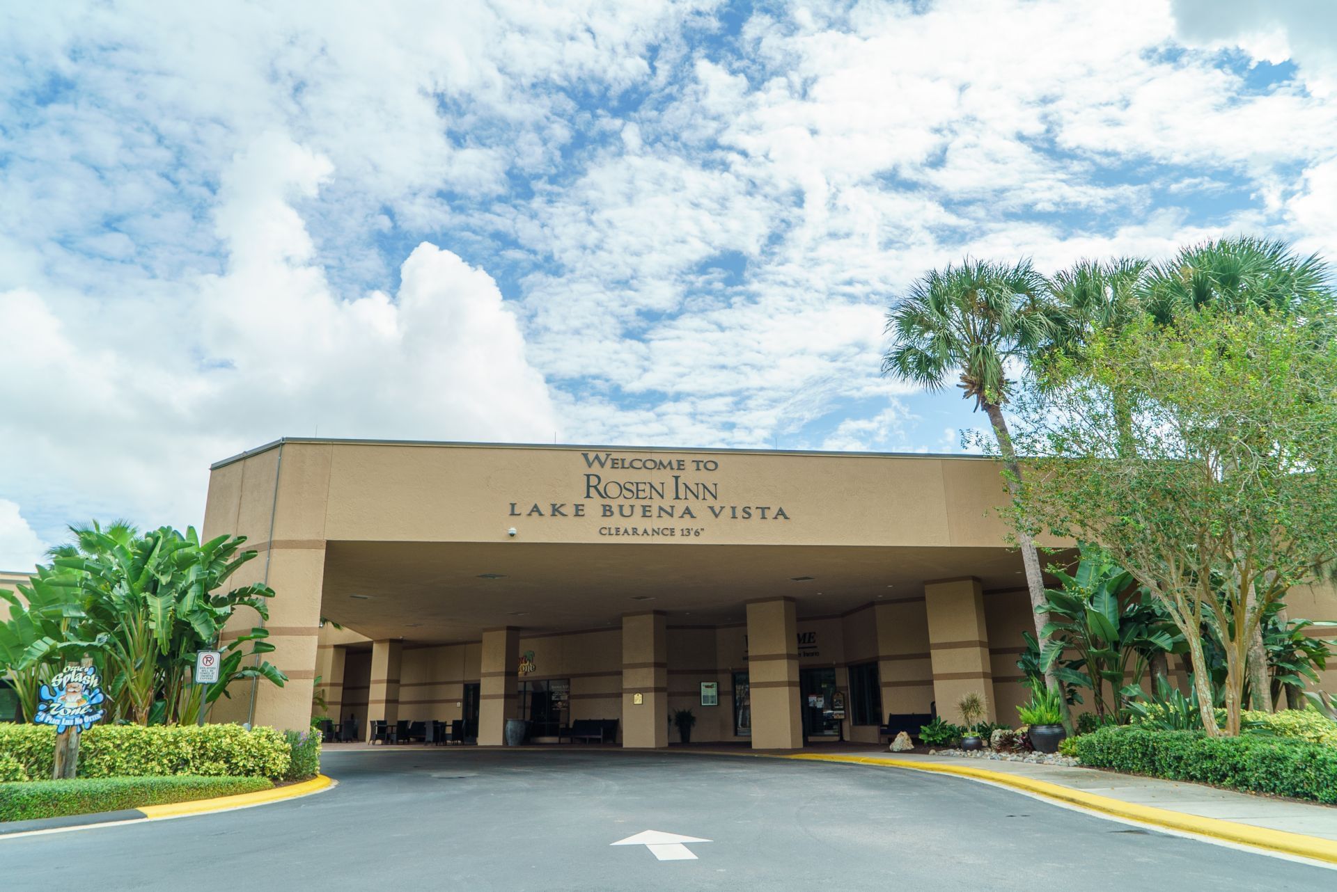 Covered entrance driveway with hotel welcome signage surrounded by palm trees at Rosen Inn Lake Buena Vista