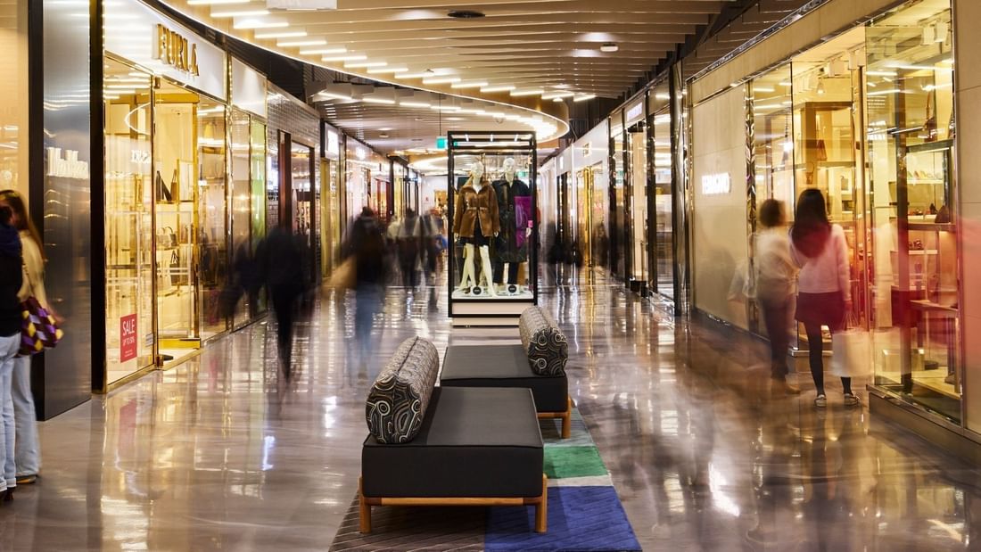 Upscale shopping corridor with illuminated storefronts and shoppers browsing luxury retail displays along polished floors