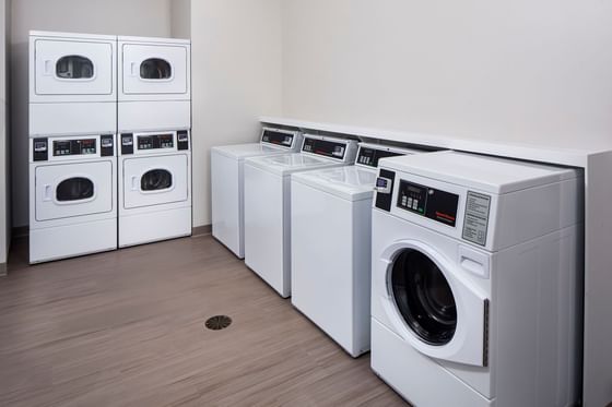 Guest laundry room with stacked dryers by washers lined along the wall under bright lights at Star Suites Vero Beach