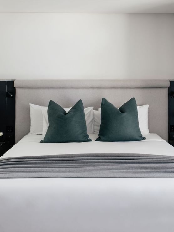 King bed at Elysium Manly with dark pillows by lamps on bedside tables, set in Elysium Suite with black panels under lighting