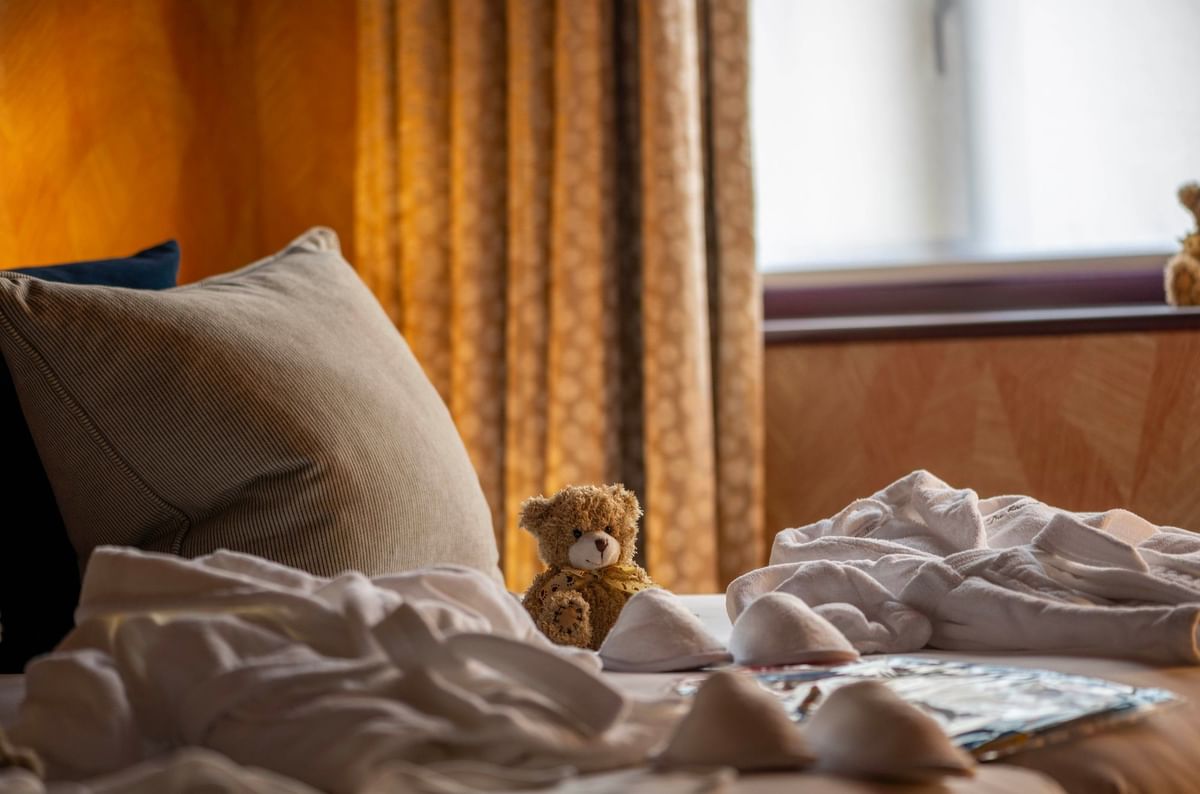 Small teddy bear sitting on a bed by plush robes and white slippers in a room at The Capital Hotel, Apartments and Townhouse