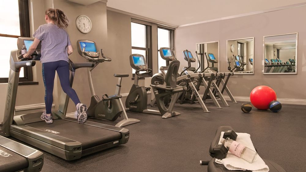 Woman running on a treadmill in a hotel fitness center with workout machines at Warwick New York