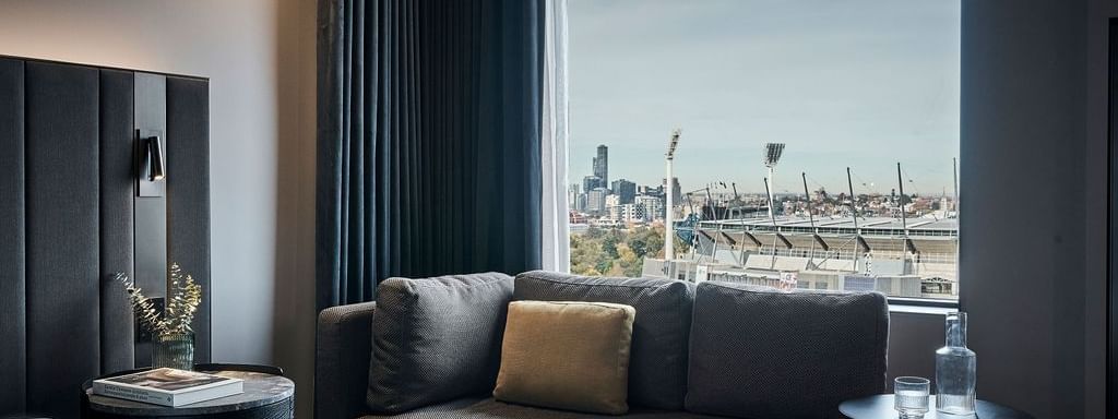 Premium Superior Room with gray sofa, city skyline views, and modern dark decor at Pullman East Melbourne