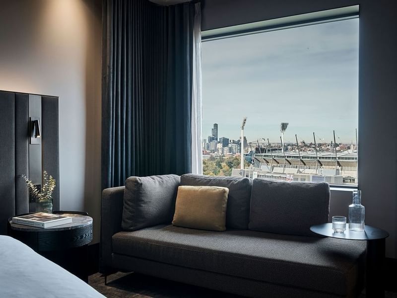 Premium Superior Room with gray sofa, city skyline views, and modern dark decor at Pullman East Melbourne