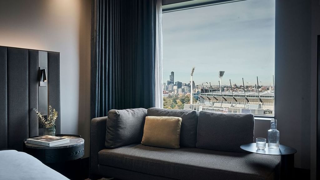 Premium Superior Room with gray sofa, city skyline views, and modern dark decor at Pullman East Melbourne