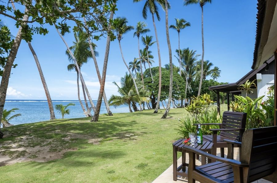 Ocean View Villa features Wooden chairs by a small table on a tiled patio under tall palm trees at Tambua Sands Beach Resort