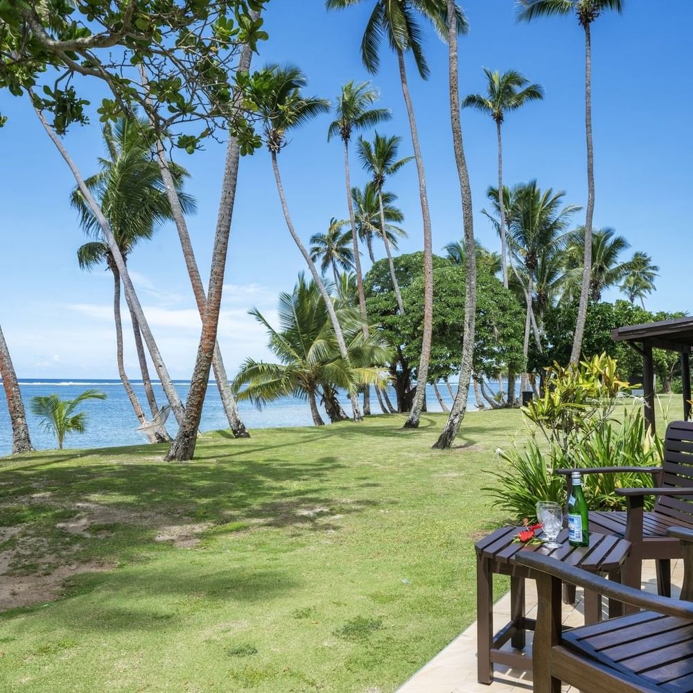 Ocean View Villa features Wooden chairs by a small table on a tiled patio under tall palm trees at Tambua Sands Beach Resort