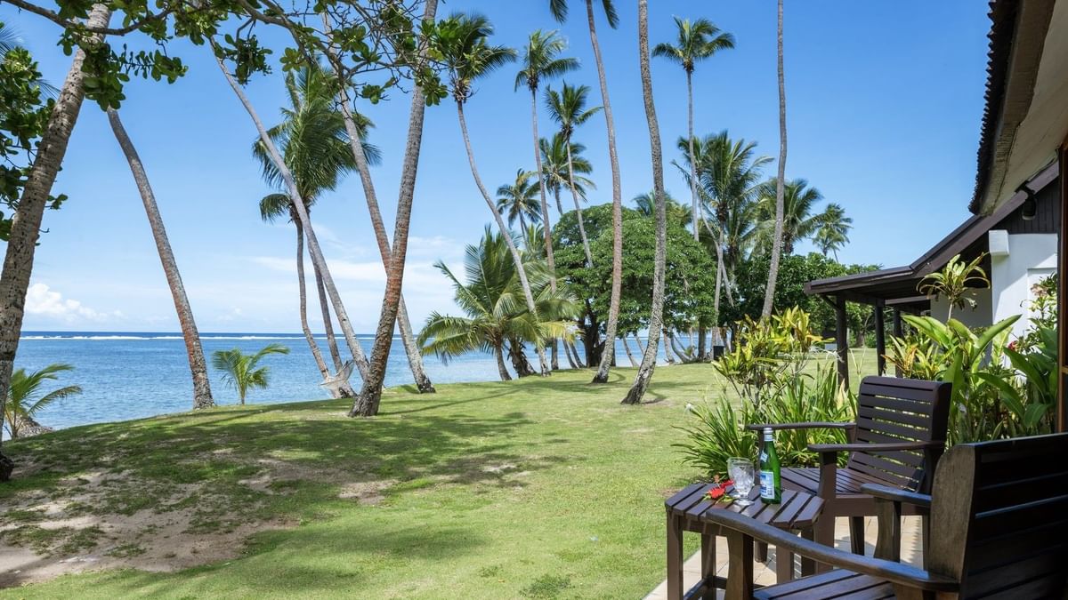 Ocean View Villa features Wooden chairs by a small table on a tiled patio under tall palm trees at Tambua Sands Beach Resort