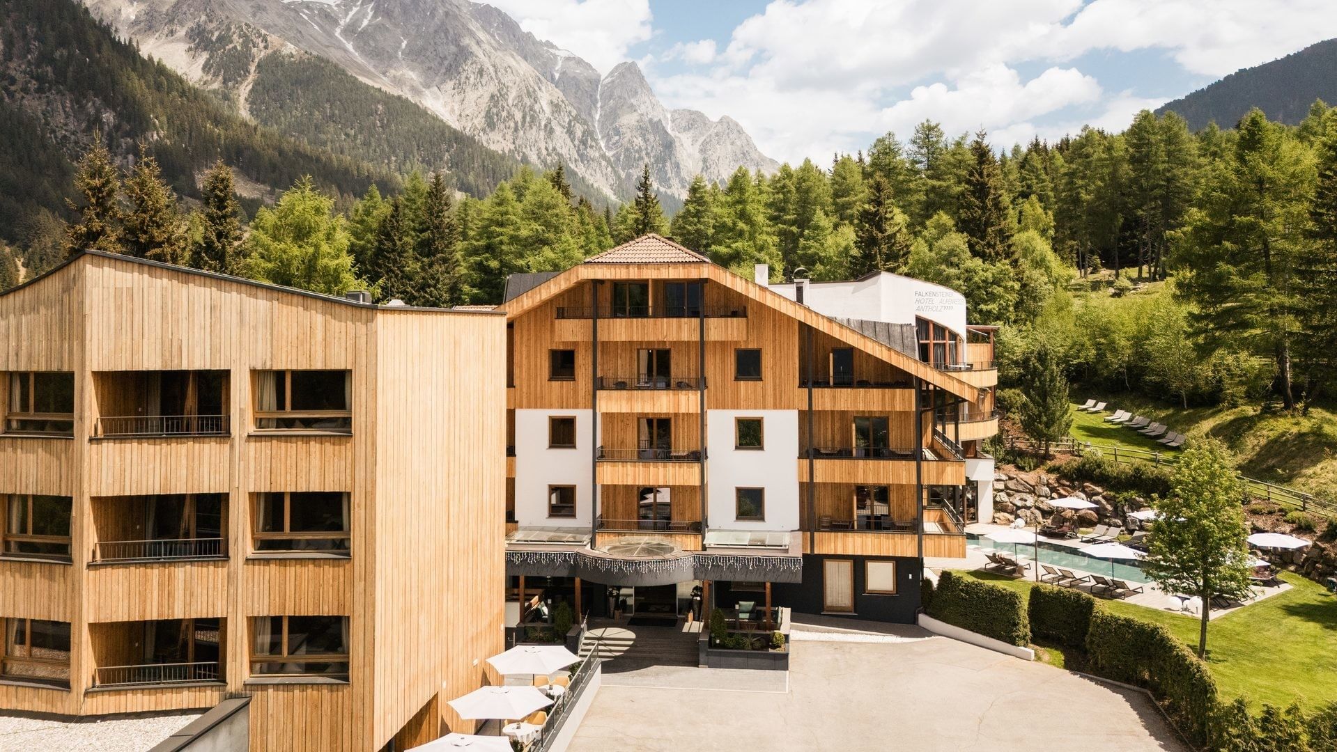 Wooden hotel building by a pine forest under a rocky mountain peak at Falkensteiner Hotel Antholz