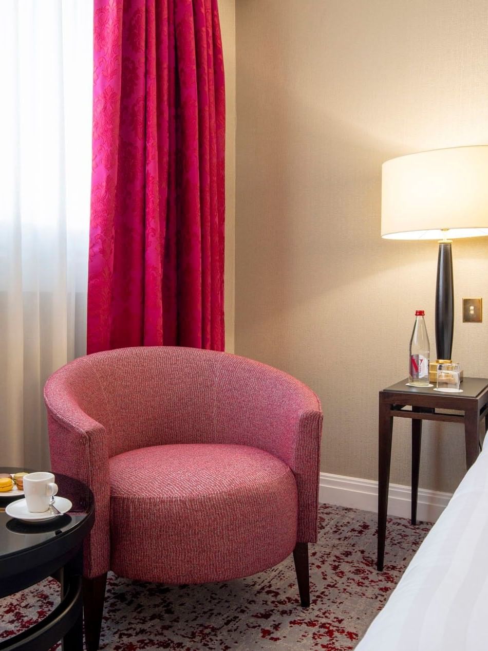 Pink armchair by a black coffee table under a floor lamp near a white bed in Superior Room at Warwick Paris Champs Elysées