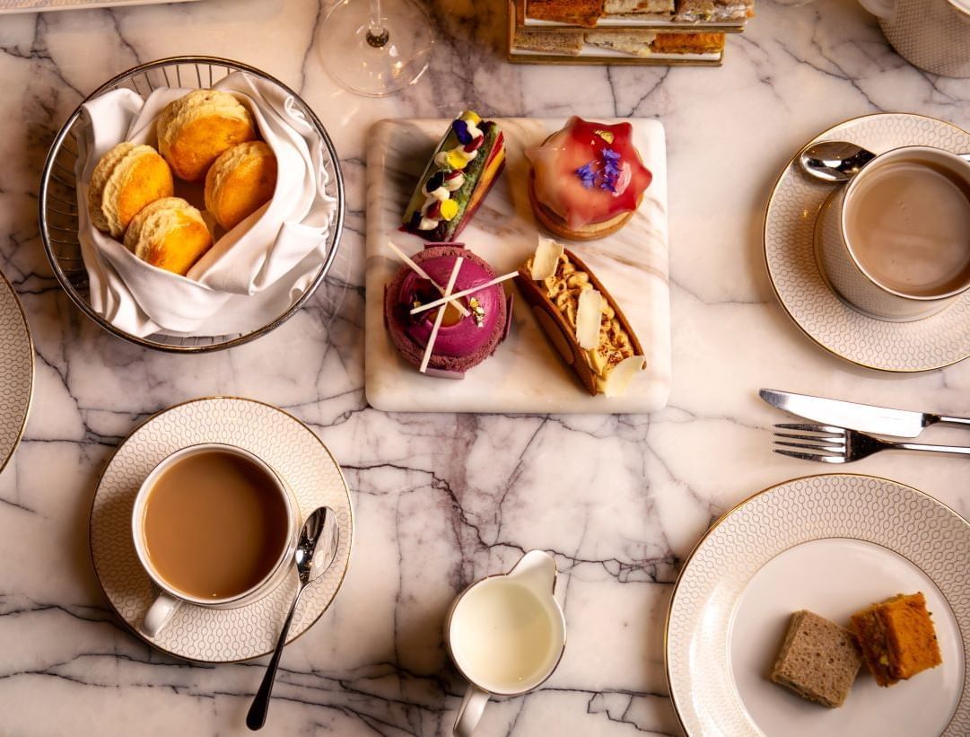 A beautiful afternoon tea spread on a marble table at The Londoner Hotel, featuring sandwiches, pastries, and champagne