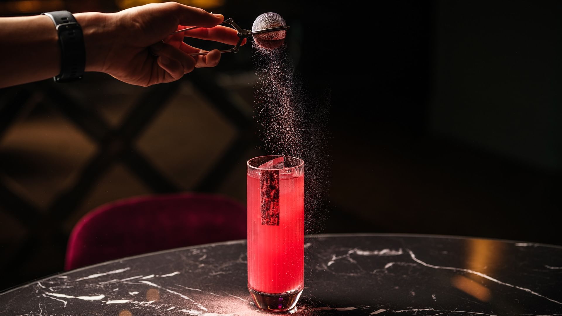 Hand-dusting powder over a red cocktail in The Monkey Bar at Falkensteiner Hotel Prague