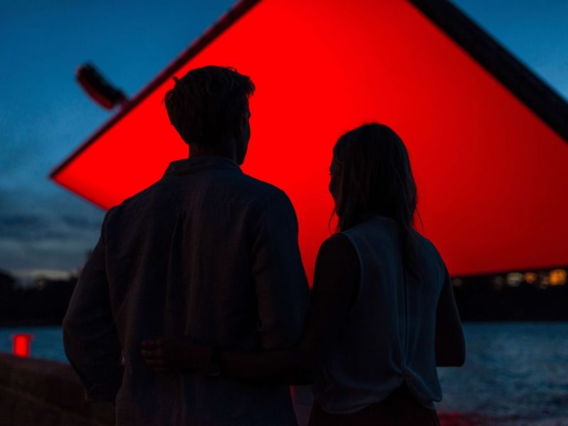 Couple watching red screen at dusk with water in background for Westpac OpenAir Cinema.