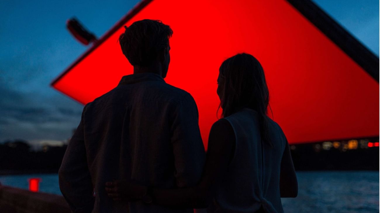 Couple watching red screen at dusk with water in background for Westpac OpenAir Cinema.