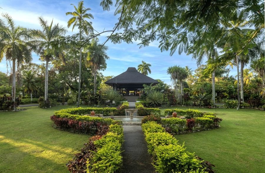 Dark pavilion by a stone fountain under palm trees and a blue sky at The Naviti Resort - Fiji