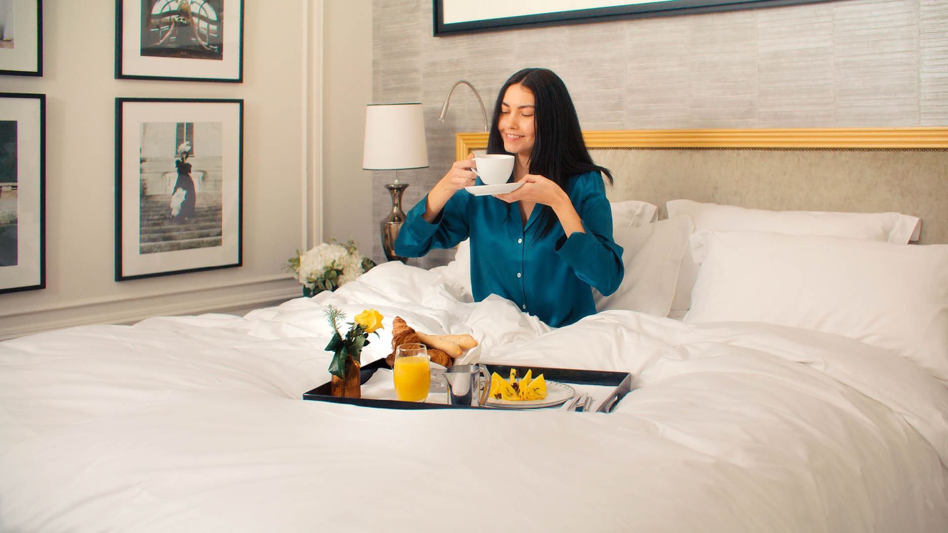 A woman in a blue shirt enjoying breakfast in bed with a tray of food at Sofitel Brisbane Central