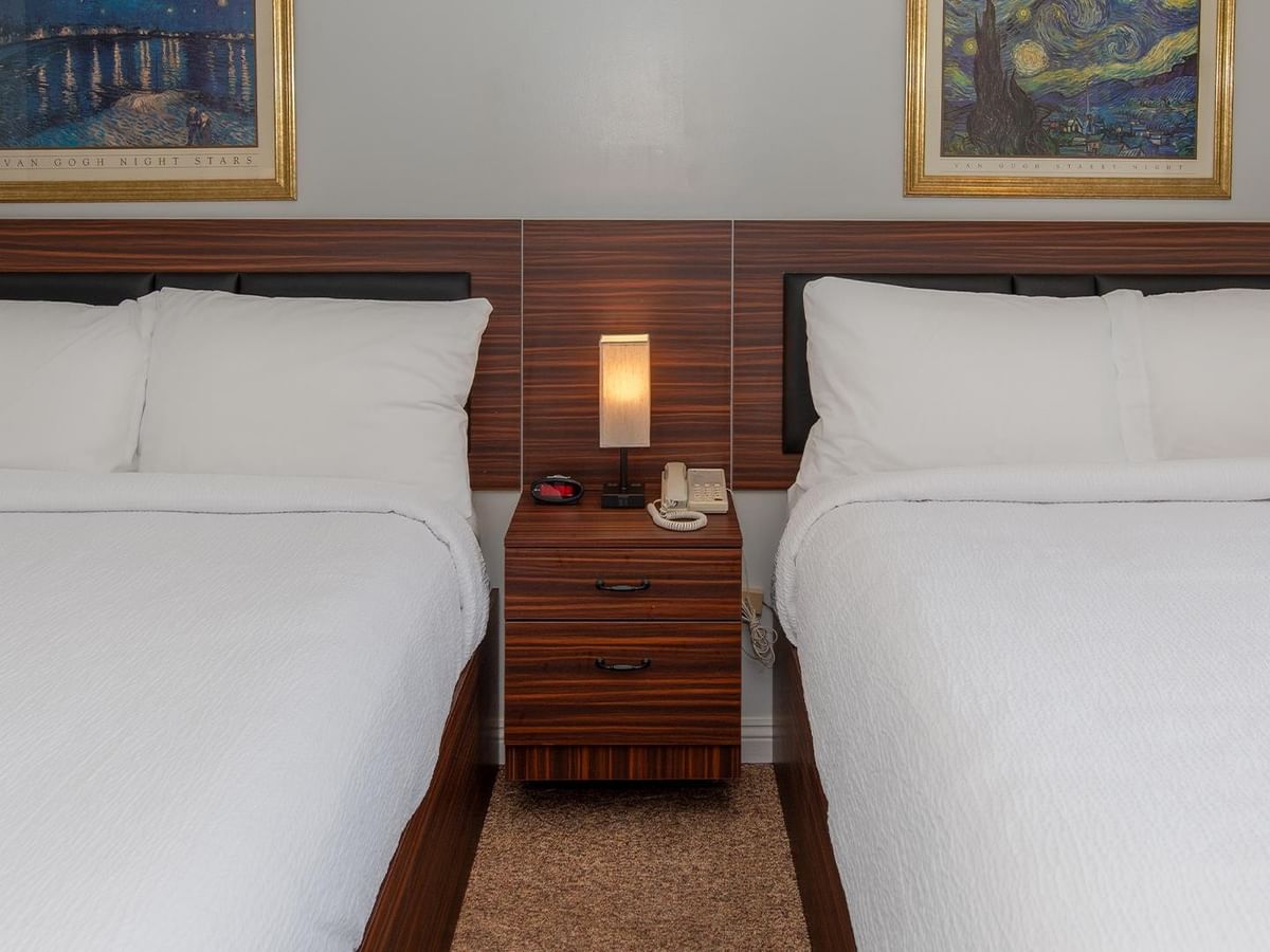 Two queen beds with bedside lighting and framed wall art