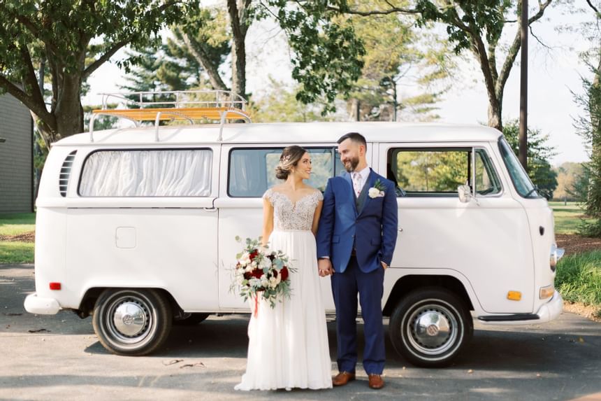 Bride and groom standing beside vintage white van in tree-lined outdoor setting at Aramark Chauncey Conference Center