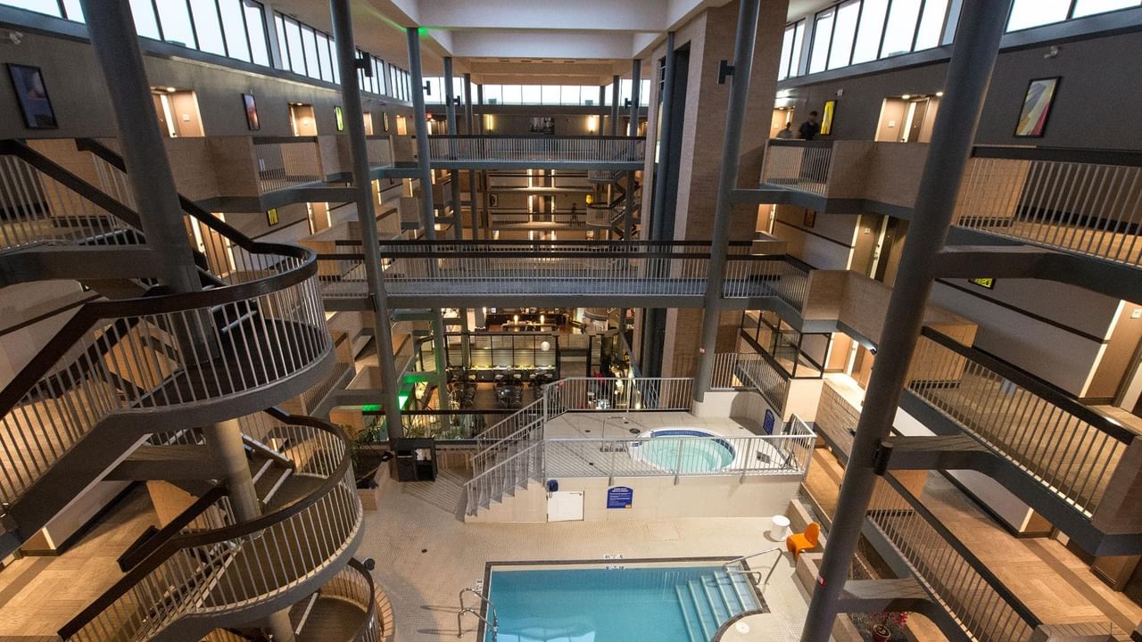 Multi-story hotel atrium with indoor pool, hot tub, and surrounding guest room balconies with warm lighting throughout.