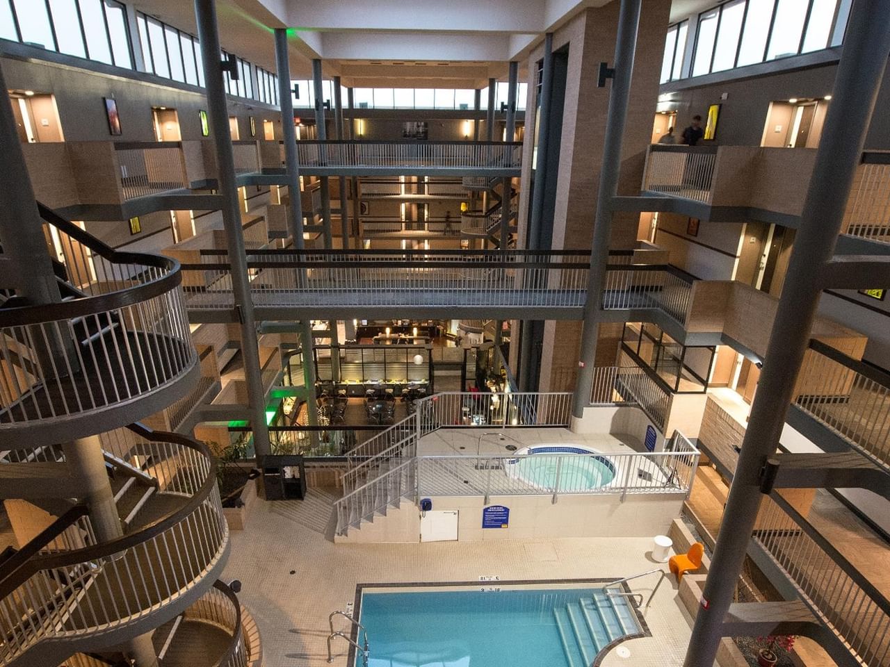 Multi-story hotel atrium with indoor pool, hot tub, and surrounding guest room balconies with warm lighting throughout.