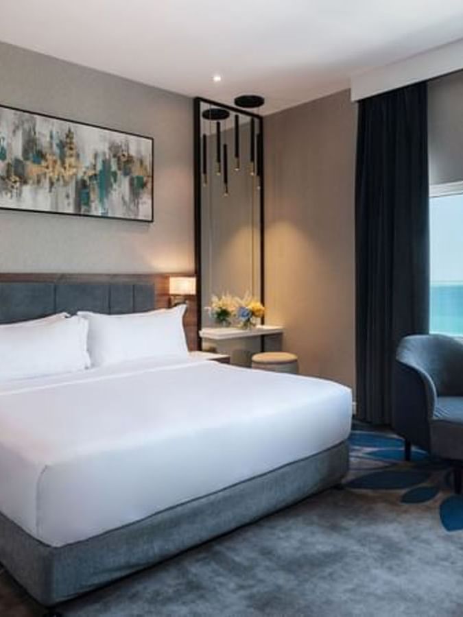 White bed by a dark armchair near a large window in Executive Room Sea View at Warwick Al Jubail