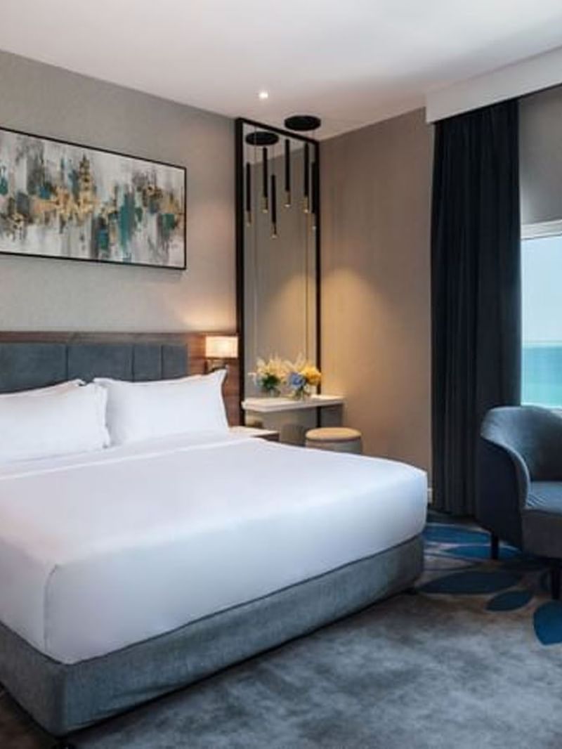 White bed by a dark armchair near a large window in Executive Room Sea View at Warwick Al Jubail