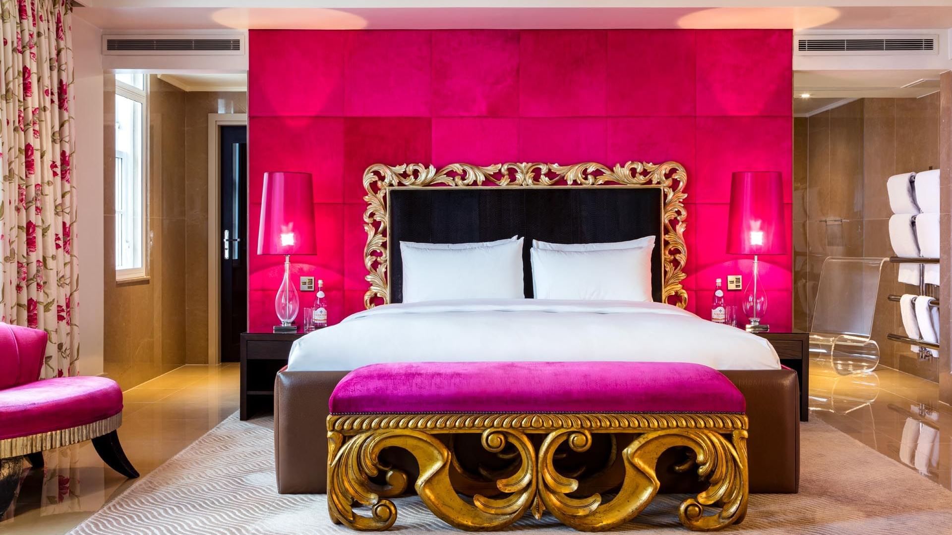 Luxurious hotel room with a bold pink theme and a plush bed in the Schiaparelli Suite at The May Fair Hotel