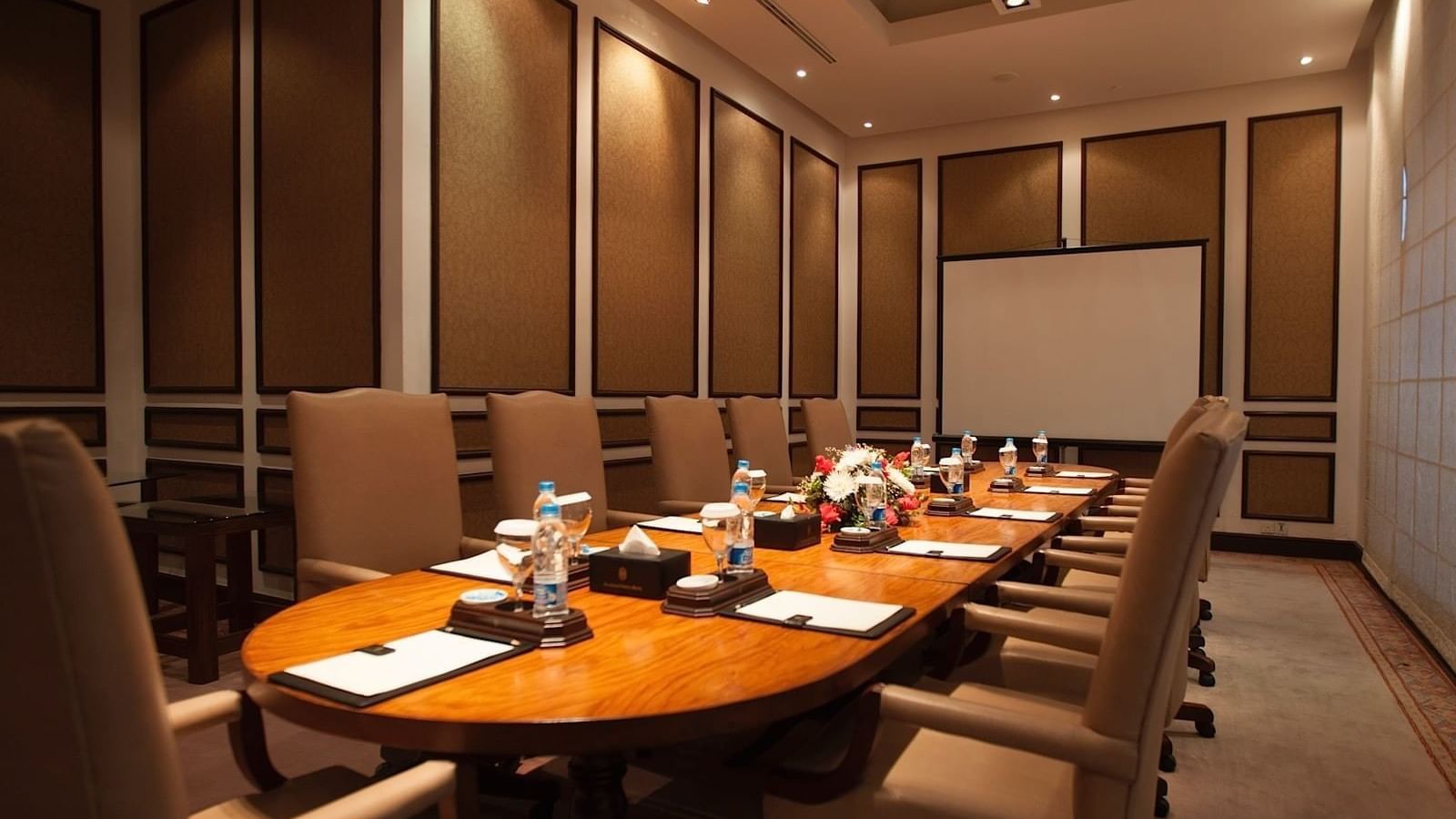 Wooden conference table with tan leather chairs and floral centerpiece in a private meeting room at Serena Hotels & Resorts