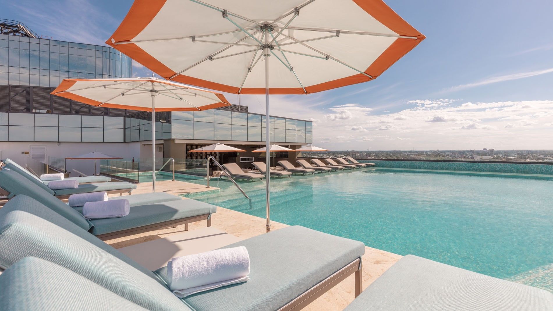 Rooftop pool deck with blue loungers, large umbrellas, and expansive horizon views at Camino Real Merida