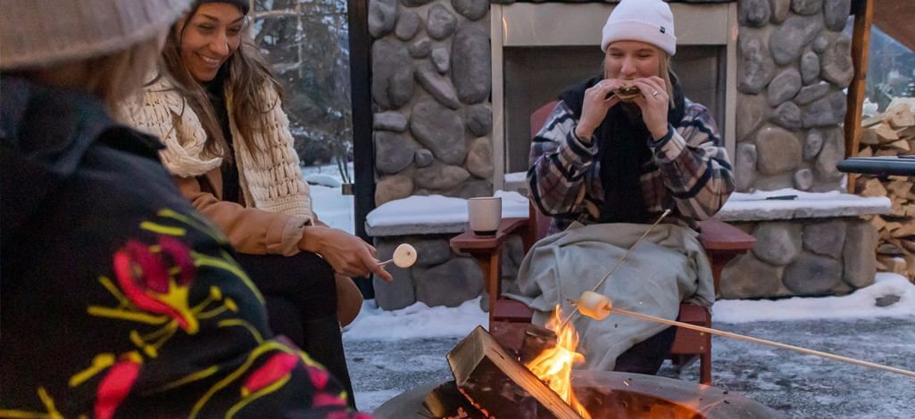 A family sits around an outdoor fire toasting marshmallows and eating s'mores.