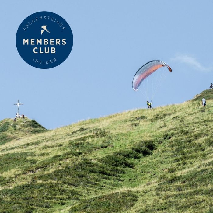 Paraglajder leti iznad zelenih brežuljaka s križem na vrhu u Falkensteiner Group