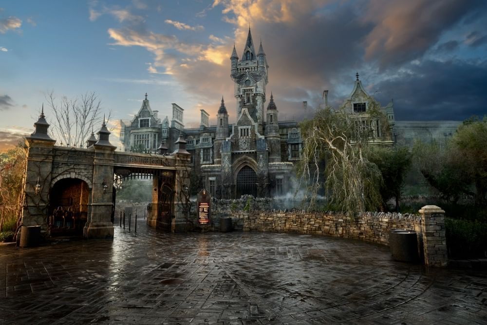 A dark lake with a stone bridge in front of a large manor with creepy turrets and mossy trees. 