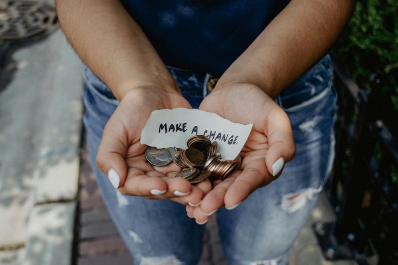 Person holding coins and a note saying MAKE A CHANGE in cupped hands near Sofitel Brisbane Central
